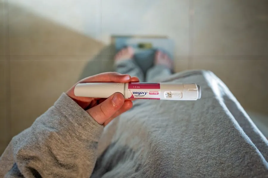 A woman stands on a scale while holding a dose of Ozempic.
